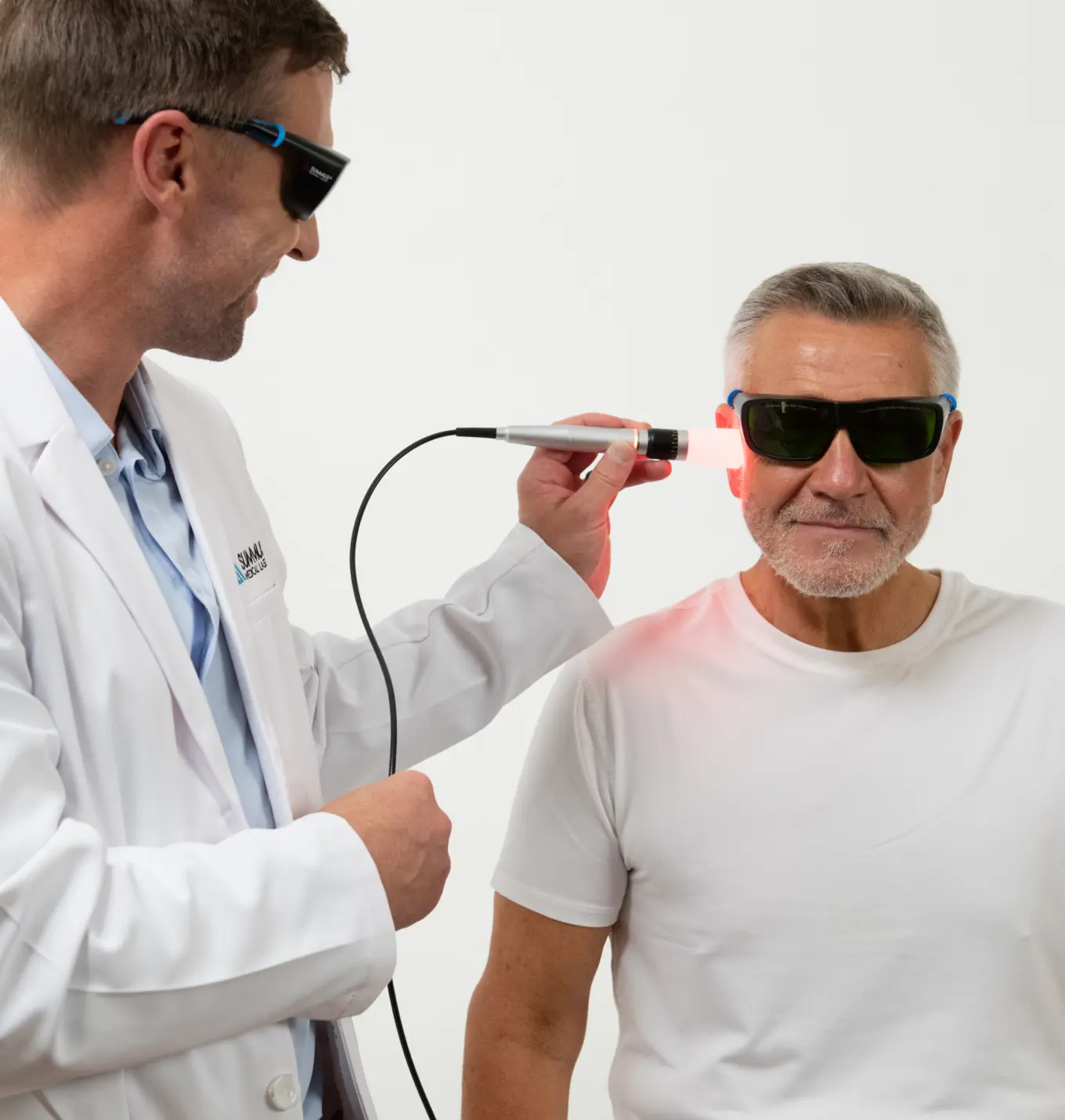 Doctor providing laser treatment to an elderly patient's jaw; both are wearing dark protective goggles