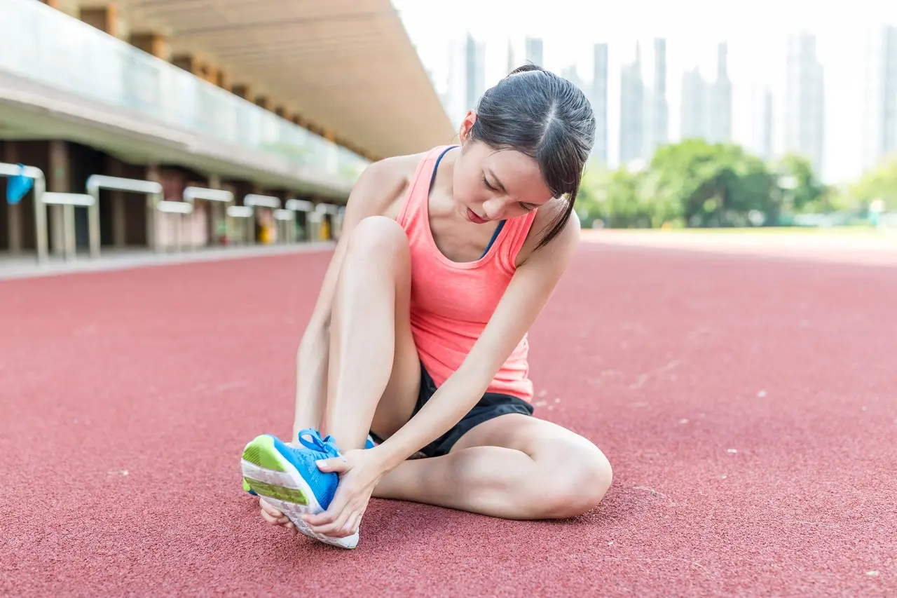 Woman runner sitting on the ground squeezing her foot